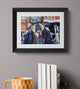 Framed artwork of a bulldog in a suit on a gray wall with books and a mug below.