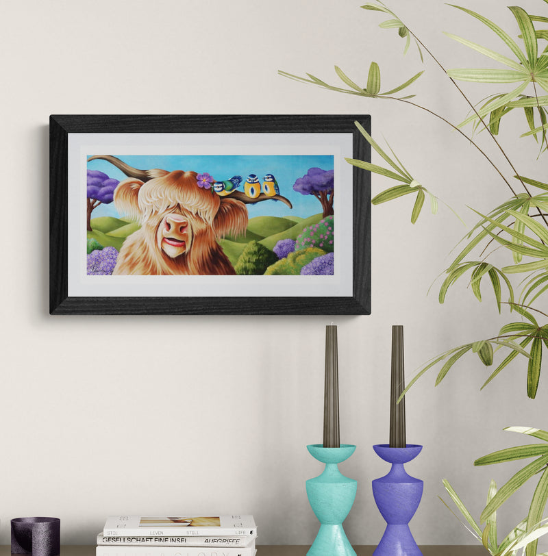 Framed artwork of a cartoon cow with a house on its head, placed on a shelf with decorative items.