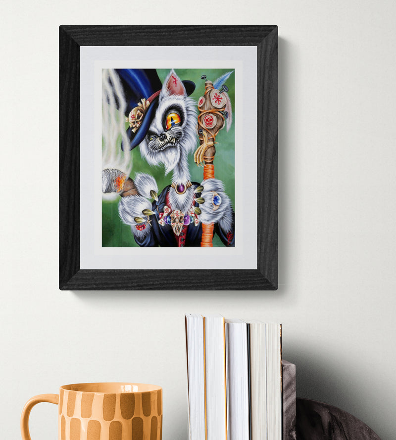 Framed artwork of a fantastical cat creature on a white wall with books and a mug below.