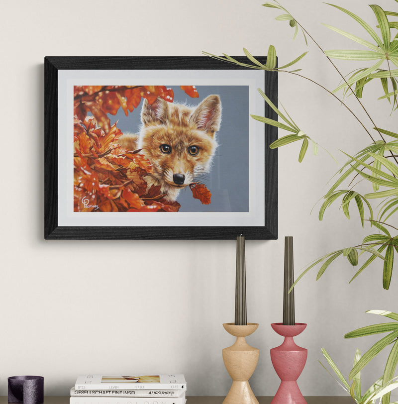 Framed artwork of a fox among autumn leaves on a wall with decorative candles and books.