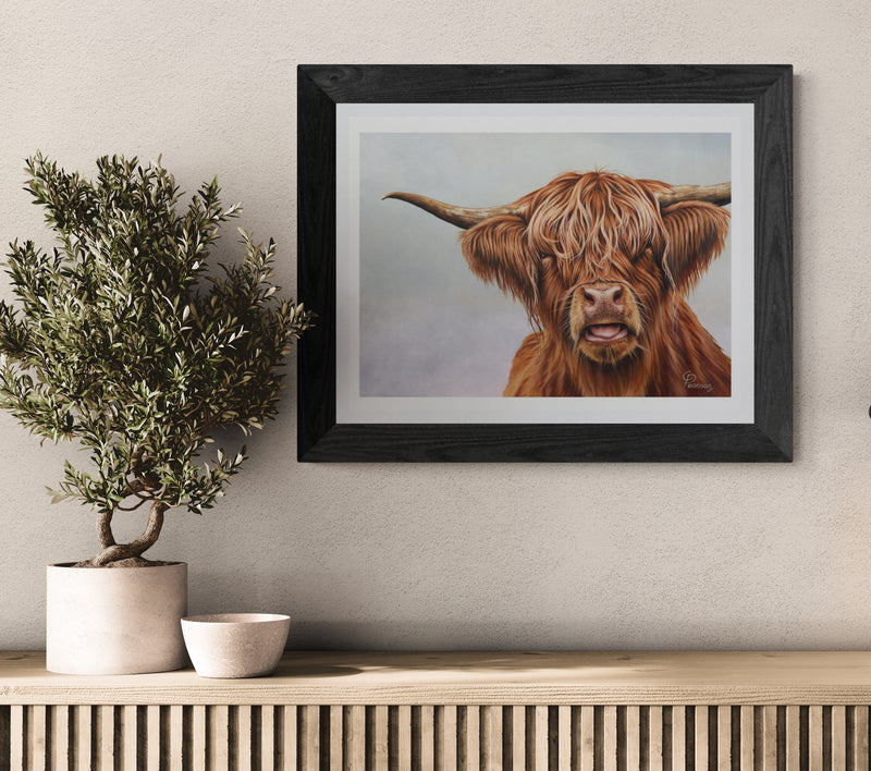 Framed artwork of a highland cow on a wall above a wooden console table with decorative items.