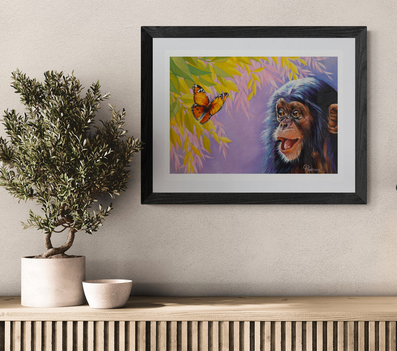 Framed artwork of a monkey and butterfly on a wall above a wooden console table.