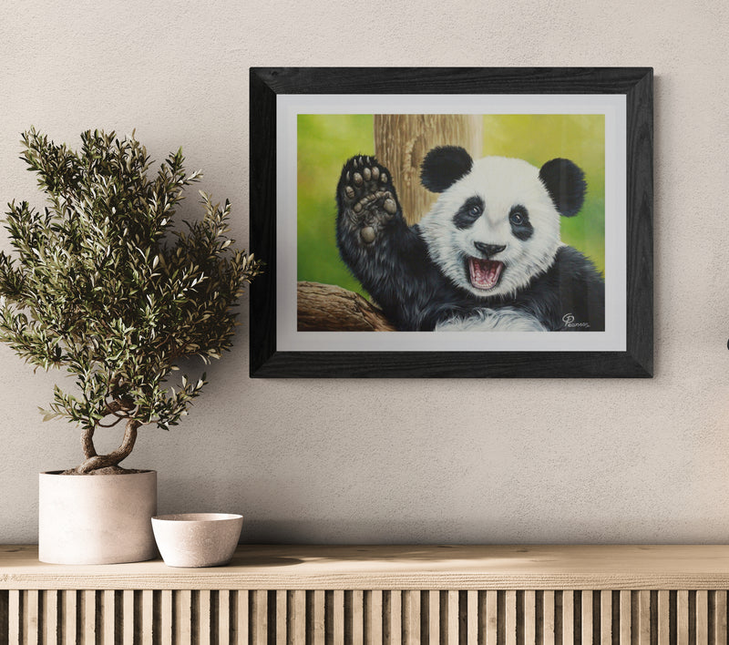Framed artwork of a panda on a wall above a wooden console table with a plant and bowl.
