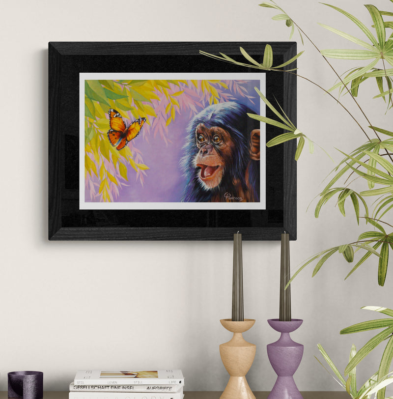 Framed painting of a monkey and butterfly on a wall with decorative candles and books below.