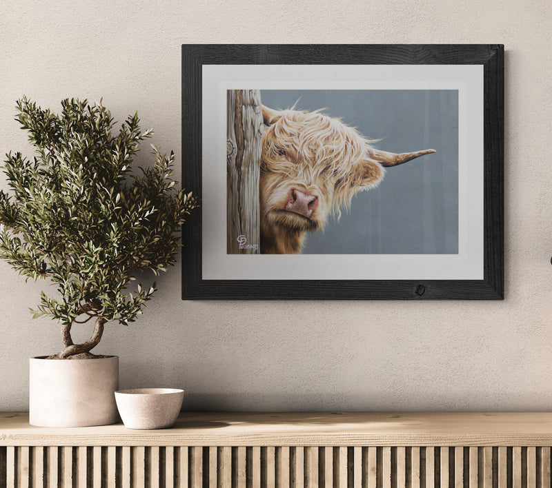 Framed picture of a Highland cow on a wall above a wooden console table with decorative items.