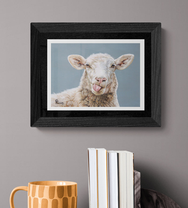 Framed picture of a sheep on a gray wall with books and a mug below.