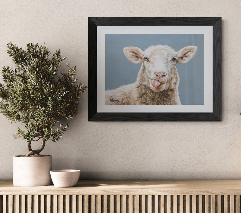 Framed picture of a sheep on a wall above a wooden console table with a plant and bowl.