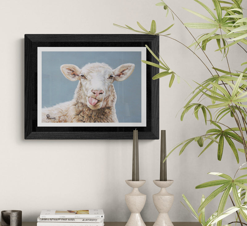 Framed picture of a lamb with a tongue sticking out on a wall with plants and decor.