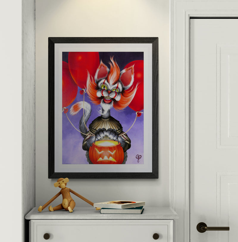 Framed artwork of a colorful haloween cat clown with red balloons on a white wall.