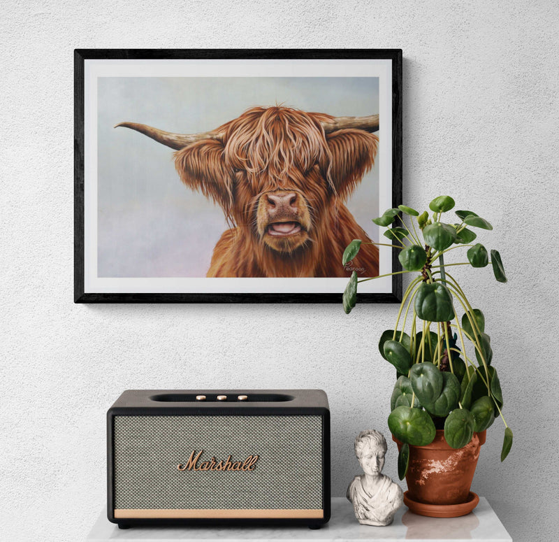 Framed artwork of a Highland cow, Marshall speaker, plant, and small statue on a white surface.