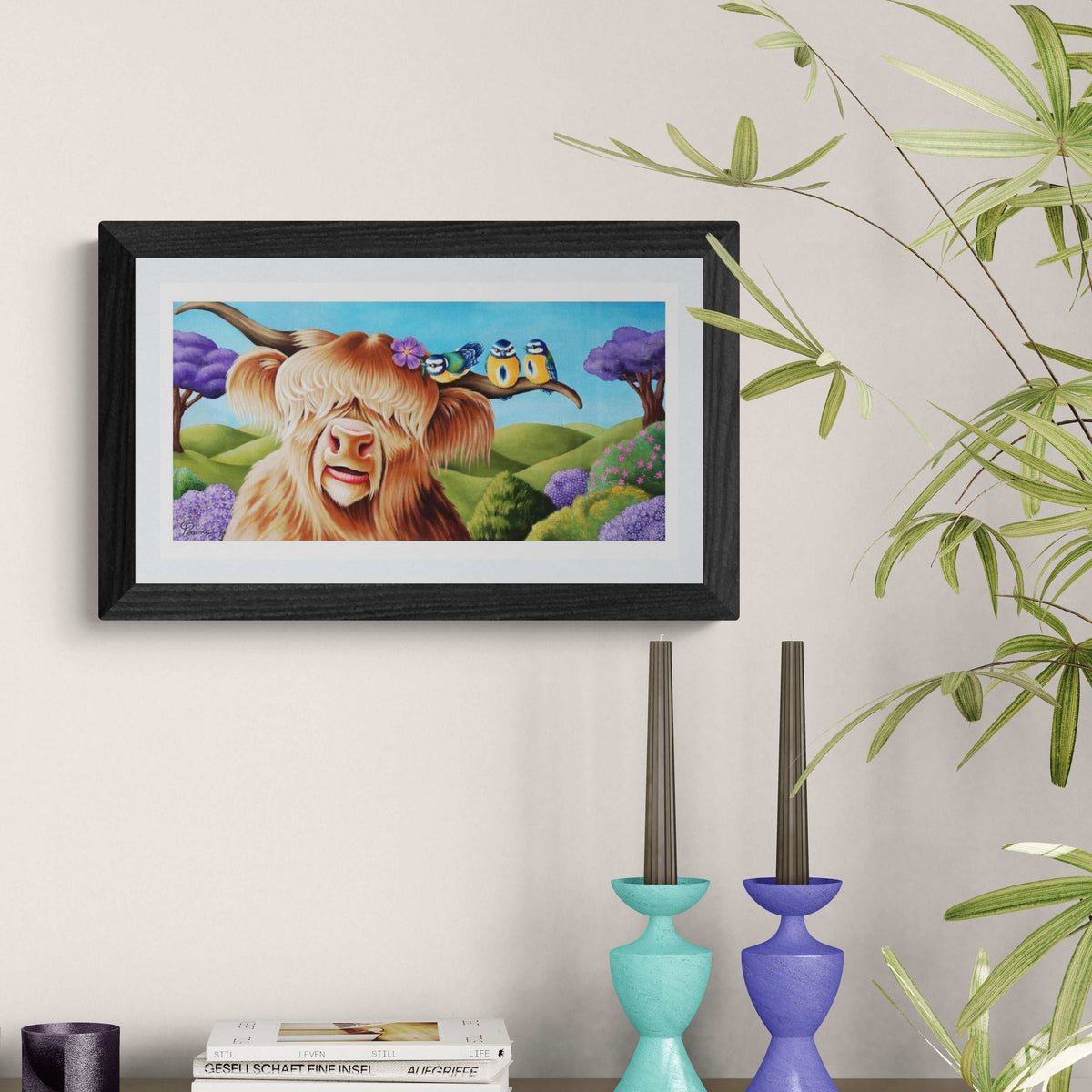 Framed artwork of a cartoon cow with a house on its head, placed on a shelf with decorative items.