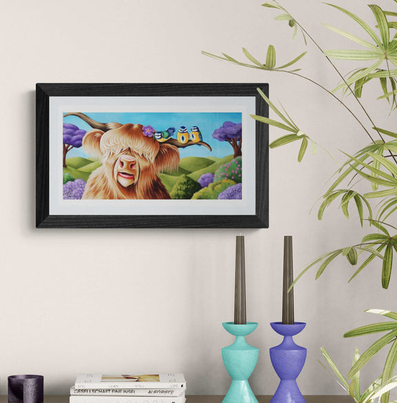 Framed artwork of a cartoon cow with a house on its head, placed on a shelf with decorative items.
