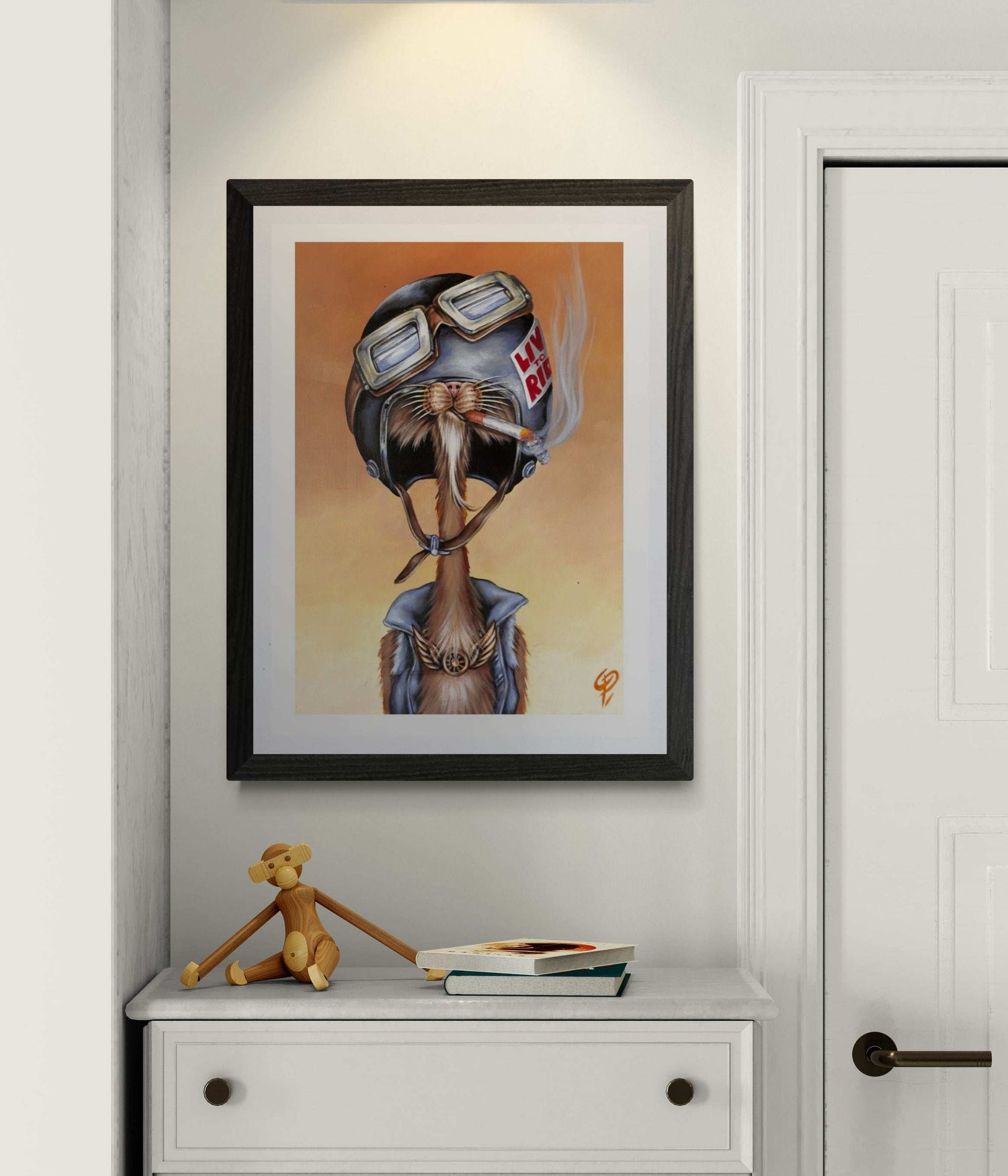 Framed artwork of a cat wearing a helmet on a wall above a white cabinet.