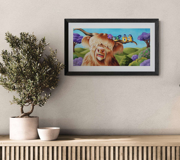 Framed artwork of a cow with a butterfly on a wall above a wooden shelf with a plant and bowl.