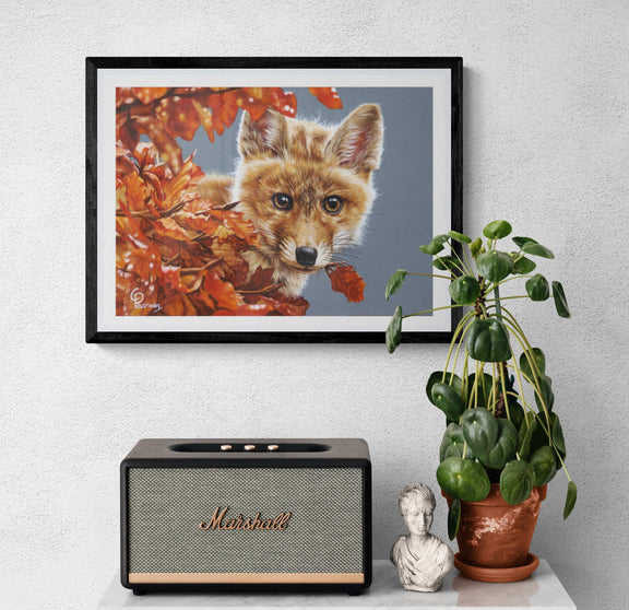 Framed artwork of a fox surrounded by autumn leaves, Marshall speaker, plant, and small statue on a white surface.