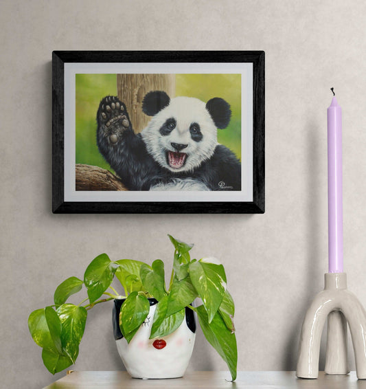 Framed artwork of a panda bear on a wall with a plant and candle in the foreground.