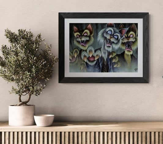 Framed artwork of three cartoon-like zombie cats on a wall above a wooden shelf with a plant and bowl.