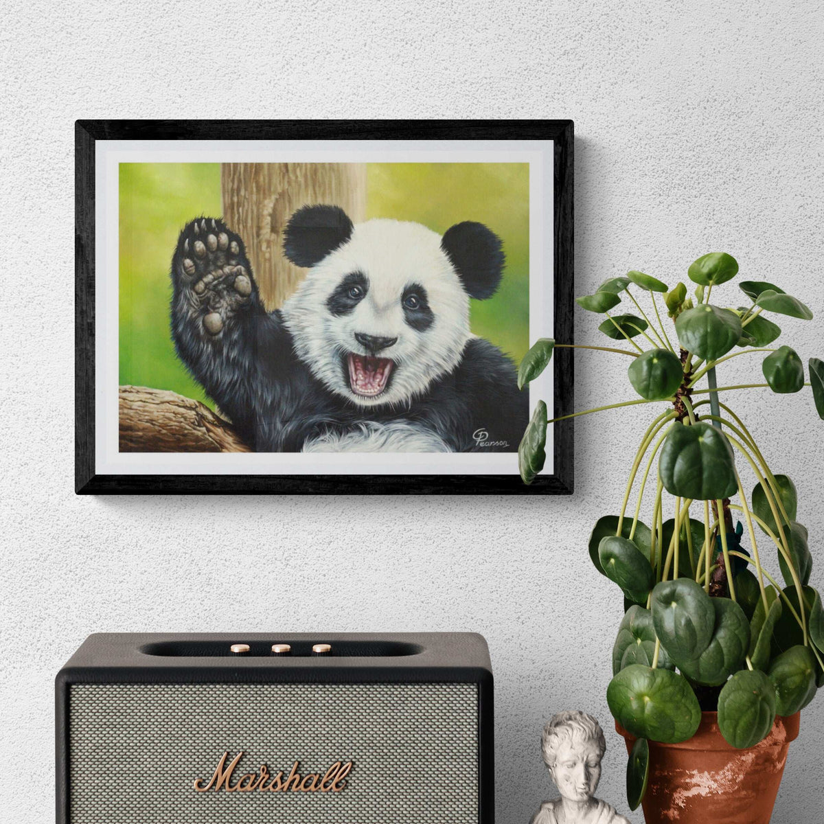 Framed picture of a panda waving, Marshall speaker, and potted plant on a white wall.