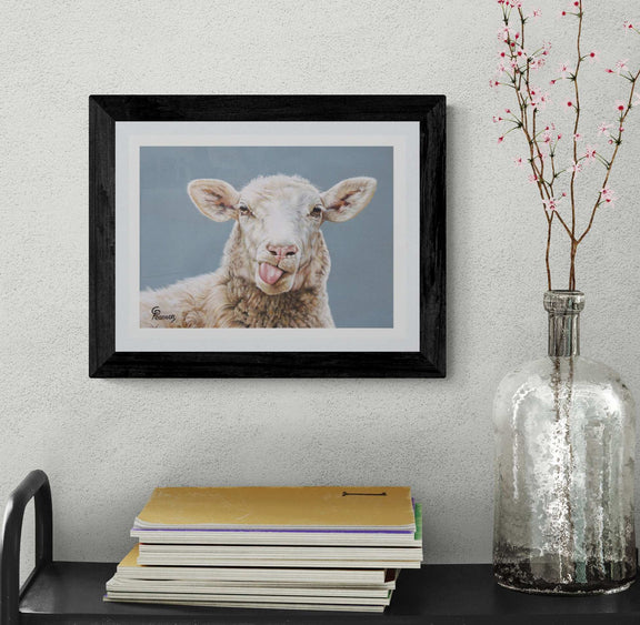 Framed picture of a sheep on a wall above a stack of books with a vase containing branches.