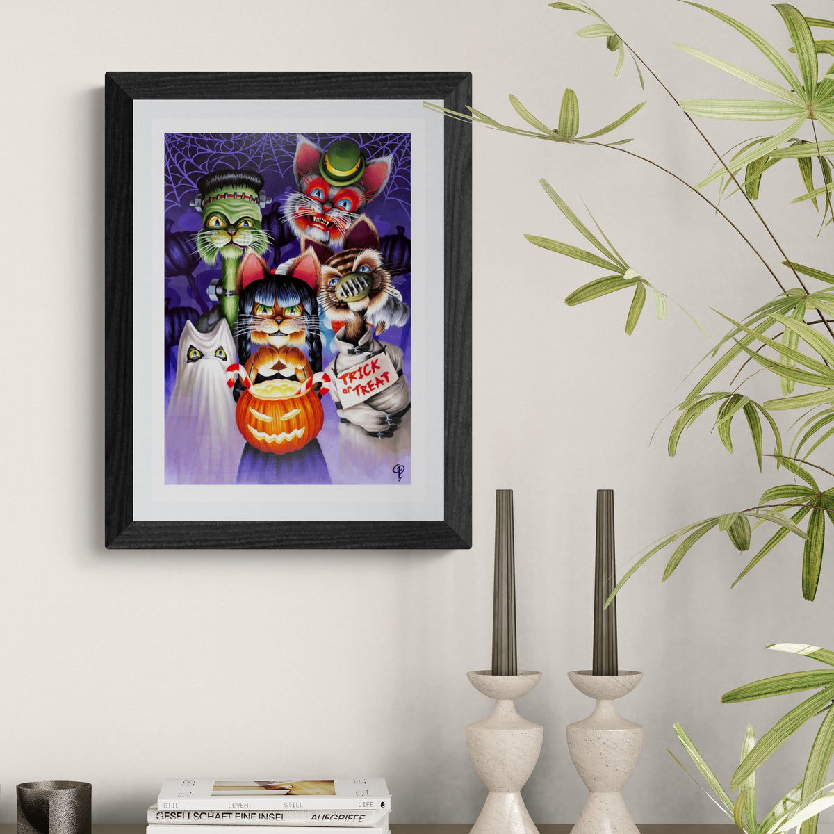 Framed Halloween-themed artwork with cats and a pumpkin on a wall above a shelf.