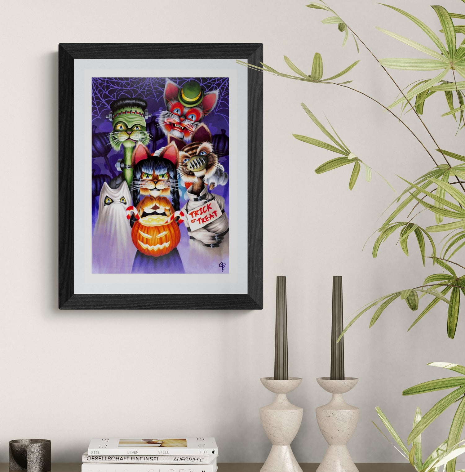 Framed Halloween-themed artwork with cats and a pumpkin on a wall above a shelf.
