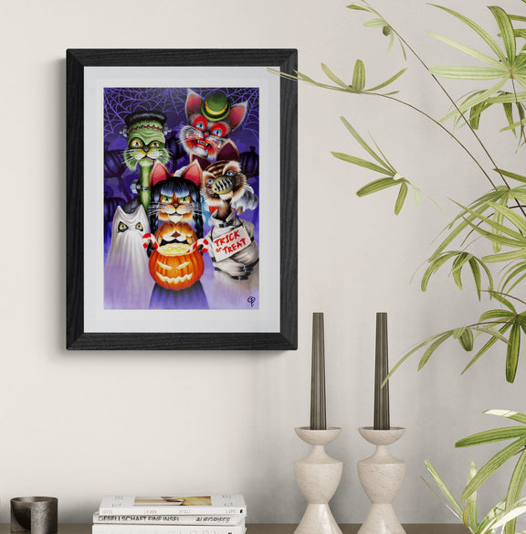 Framed Halloween-themed artwork with cats and a pumpkin on a wall above a shelf.