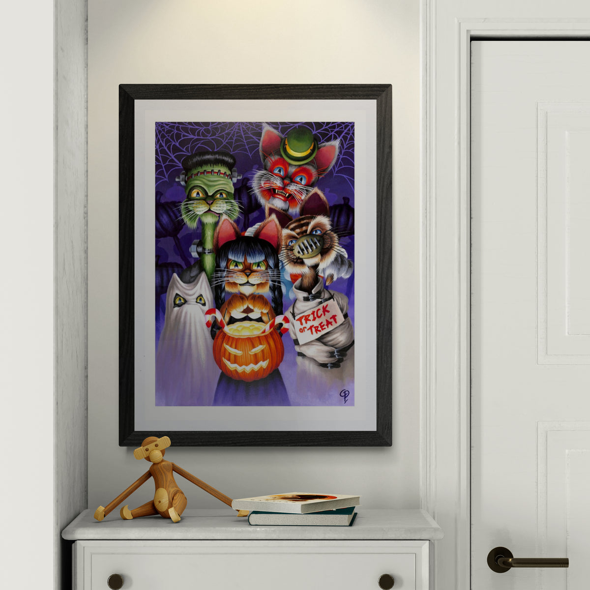 Framed Halloween-themed artwork with cartoon cat  characters on a white wall.