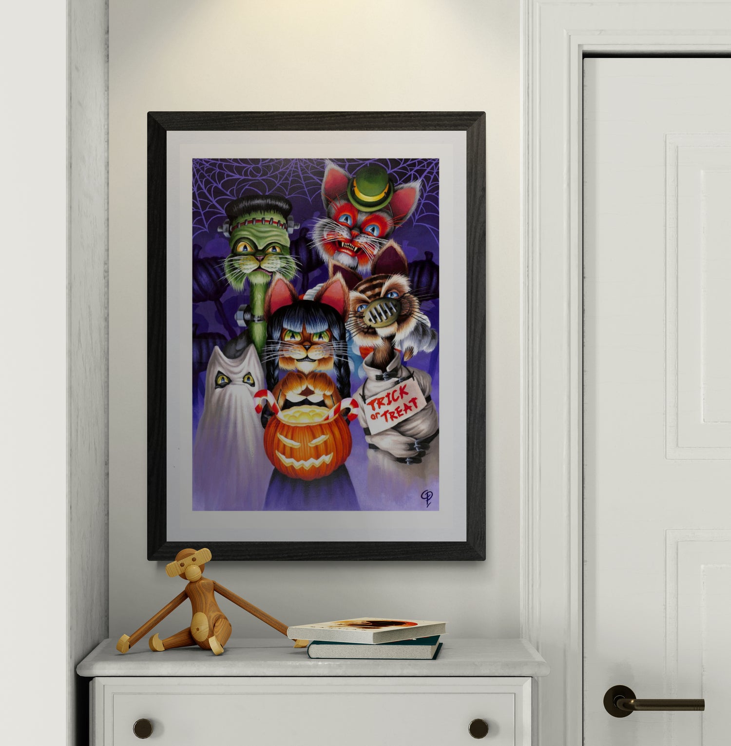 Framed Halloween-themed artwork with cartoon cat  characters on a white wall.