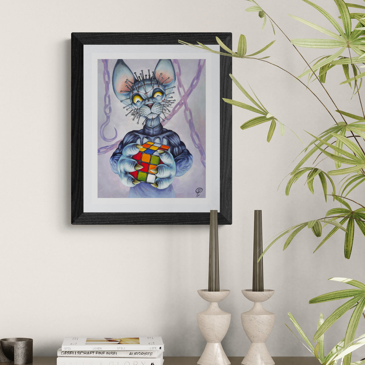 Framed artwork of a cat creature holding a Rubik's Cube on a wall with decorative elements.
