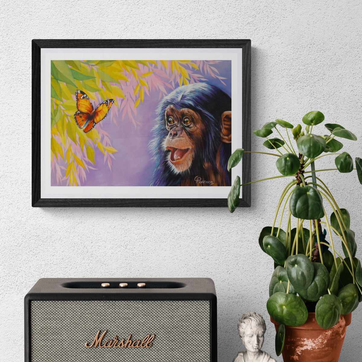 Framed artwork of a chimpanzee and butterfly on a wall above a Marshall speaker with a plant beside it.