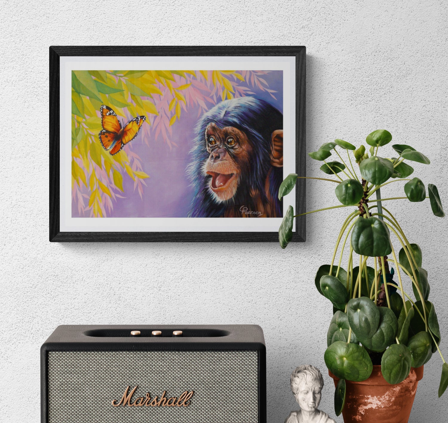 Framed artwork of a chimpanzee and butterfly on a wall above a Marshall speaker with a plant beside it.