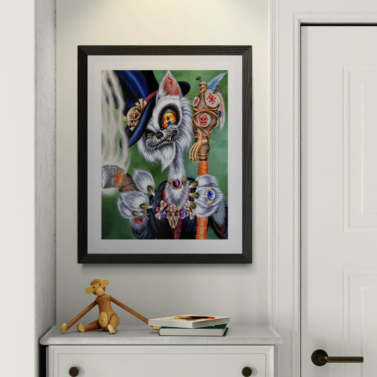 Framed artwork of a colorful cat creature with a staff on a white wall.