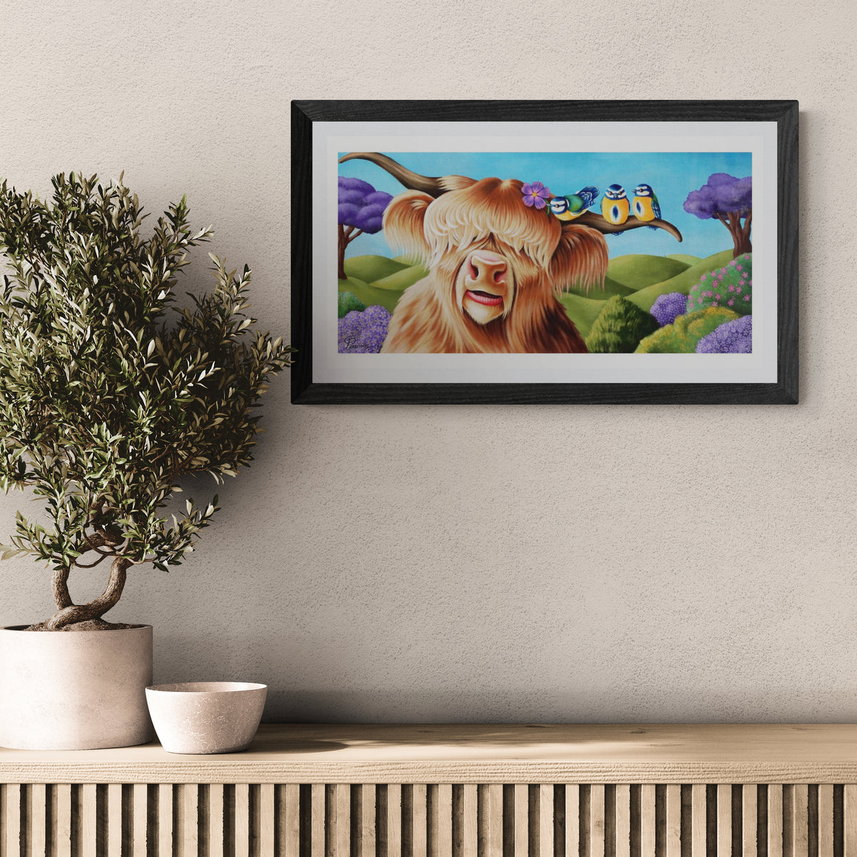 Framed artwork of a cow with a butterfly on a wall above a wooden shelf with a plant and bowl.