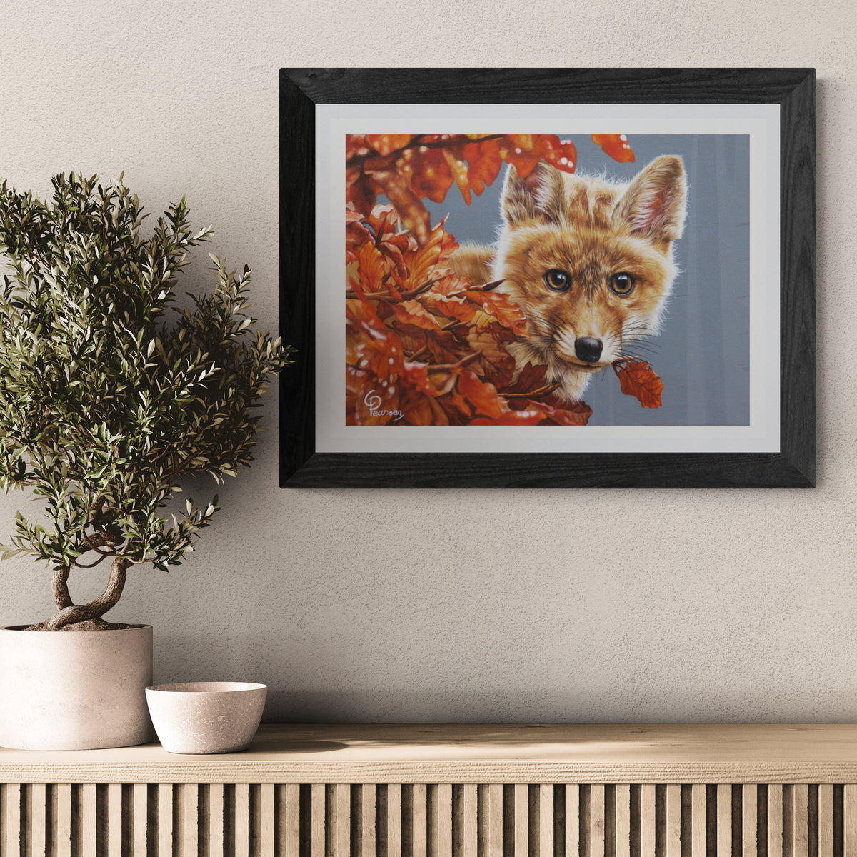 Framed artwork of a fox surrounded by autumn leaves on a wall above a wooden console table.
