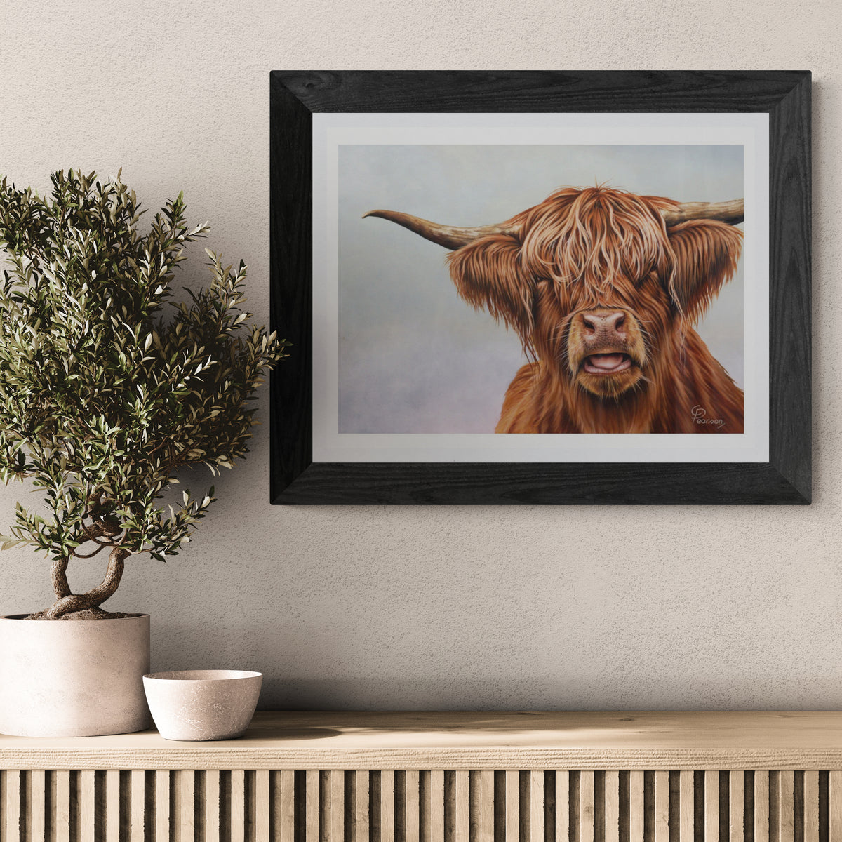 Framed artwork of a highland cow on a wall above a wooden console table with decorative items.
