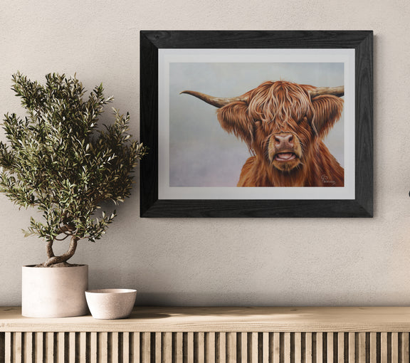 Framed artwork of a highland cow on a wall above a wooden console table with decorative items.