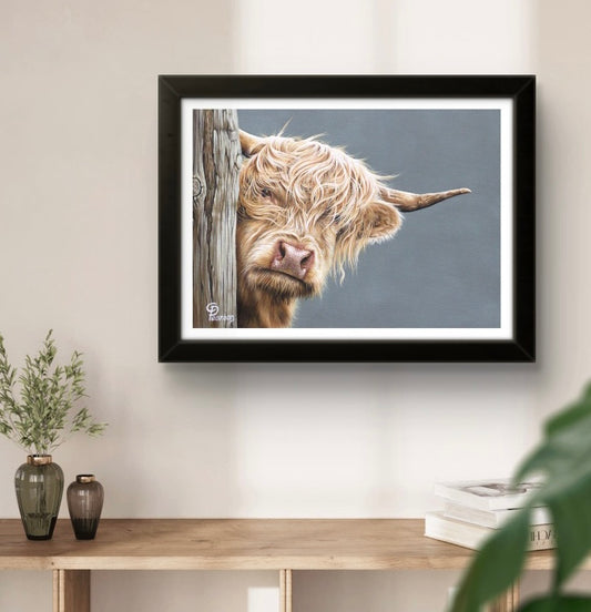 Framed artwork of a highland cow peeking from behind a wooden post on a wall.