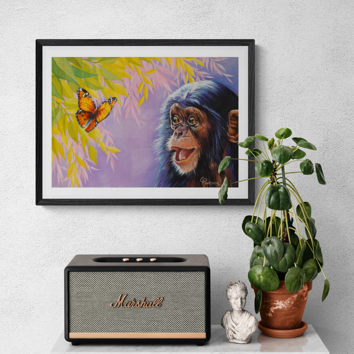 Framed artwork of a monkey and butterfly on a wall above a Marshall speaker and plant.