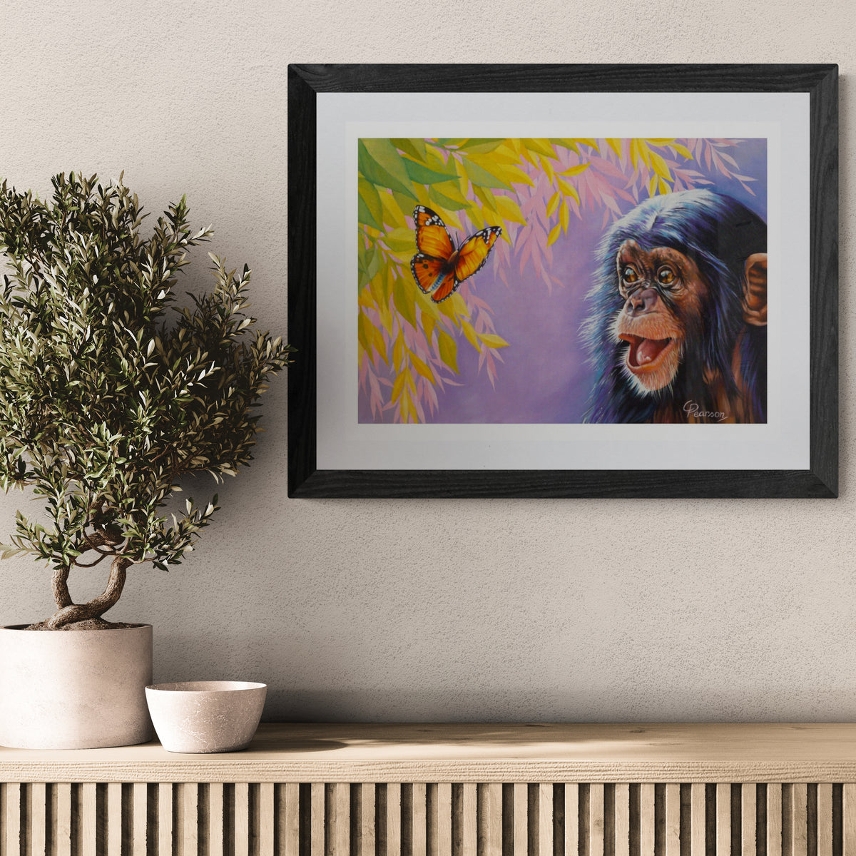 Framed artwork of a monkey and butterfly on a wall above a wooden console table.