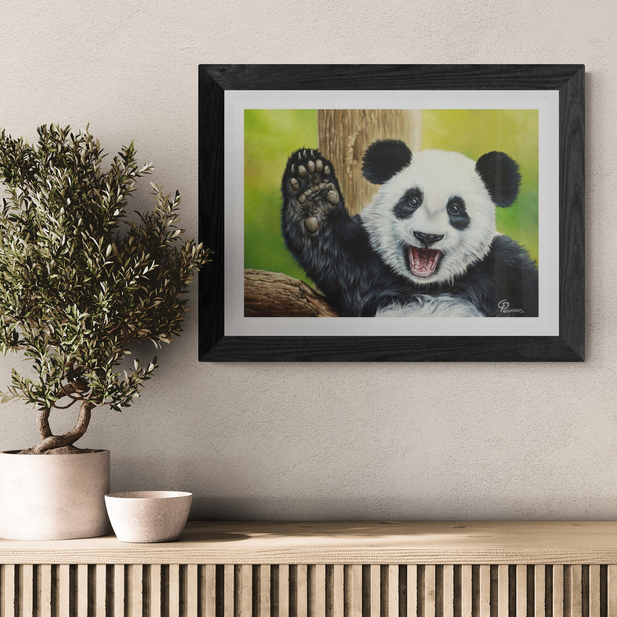 Framed artwork of a panda on a wall above a wooden console table with a plant and bowl.