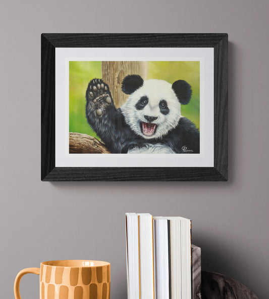 Framed artwork of a panda waving on a gray wall with books and a mug below.