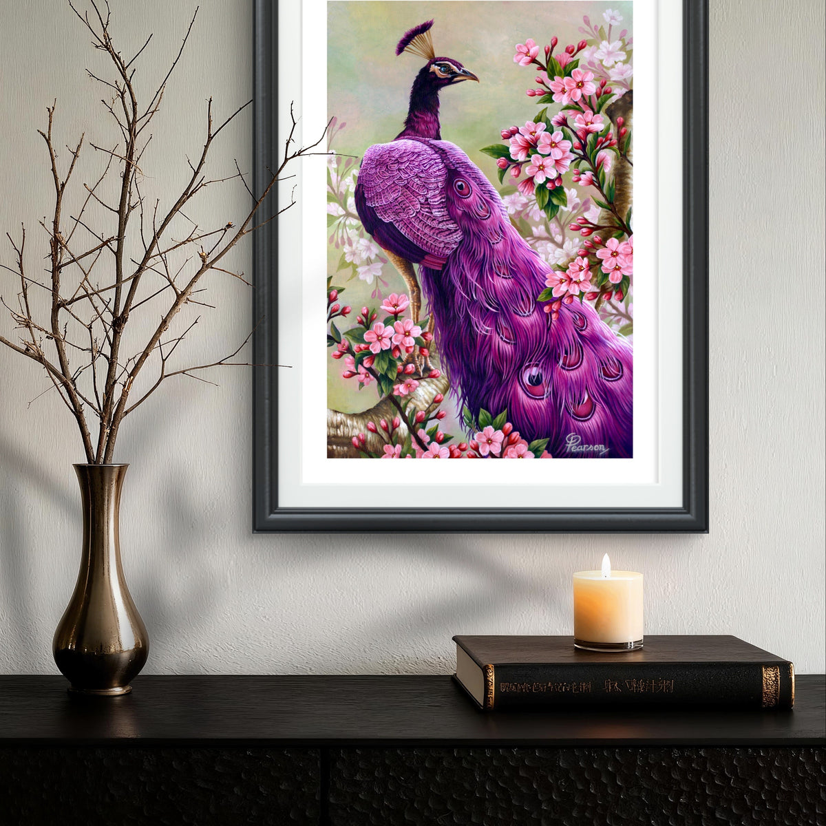 Framed artwork of a purple peacock among flowers on a wall above a dark surface with a candle and vase.
