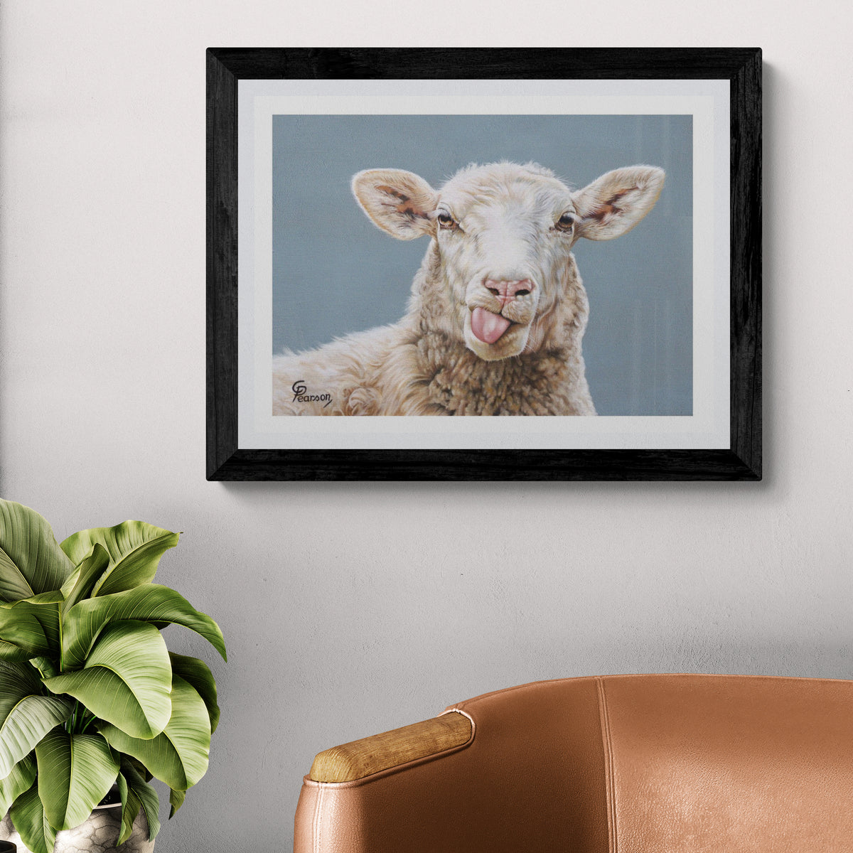 Framed artwork of a sheep with a tongue sticking out on a wall above a brown chair and plant.
