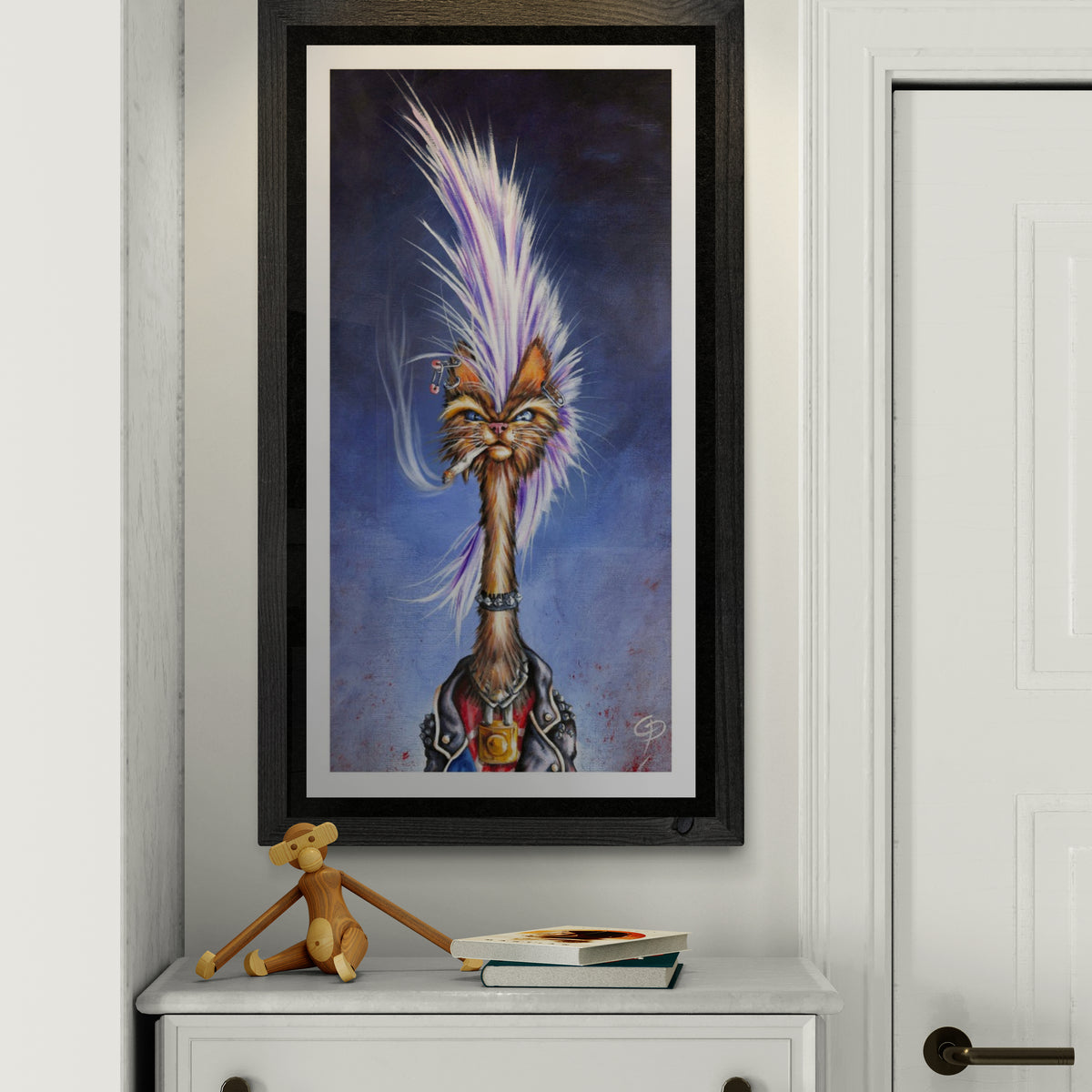 Framed artwork of a stylized cat with a feathered headdress on a white wall.