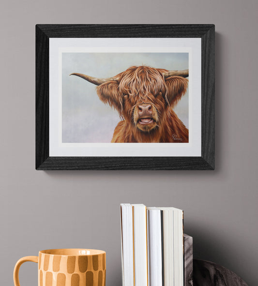 Framed painting of a highland cow on a gray wall with books and a mug below.