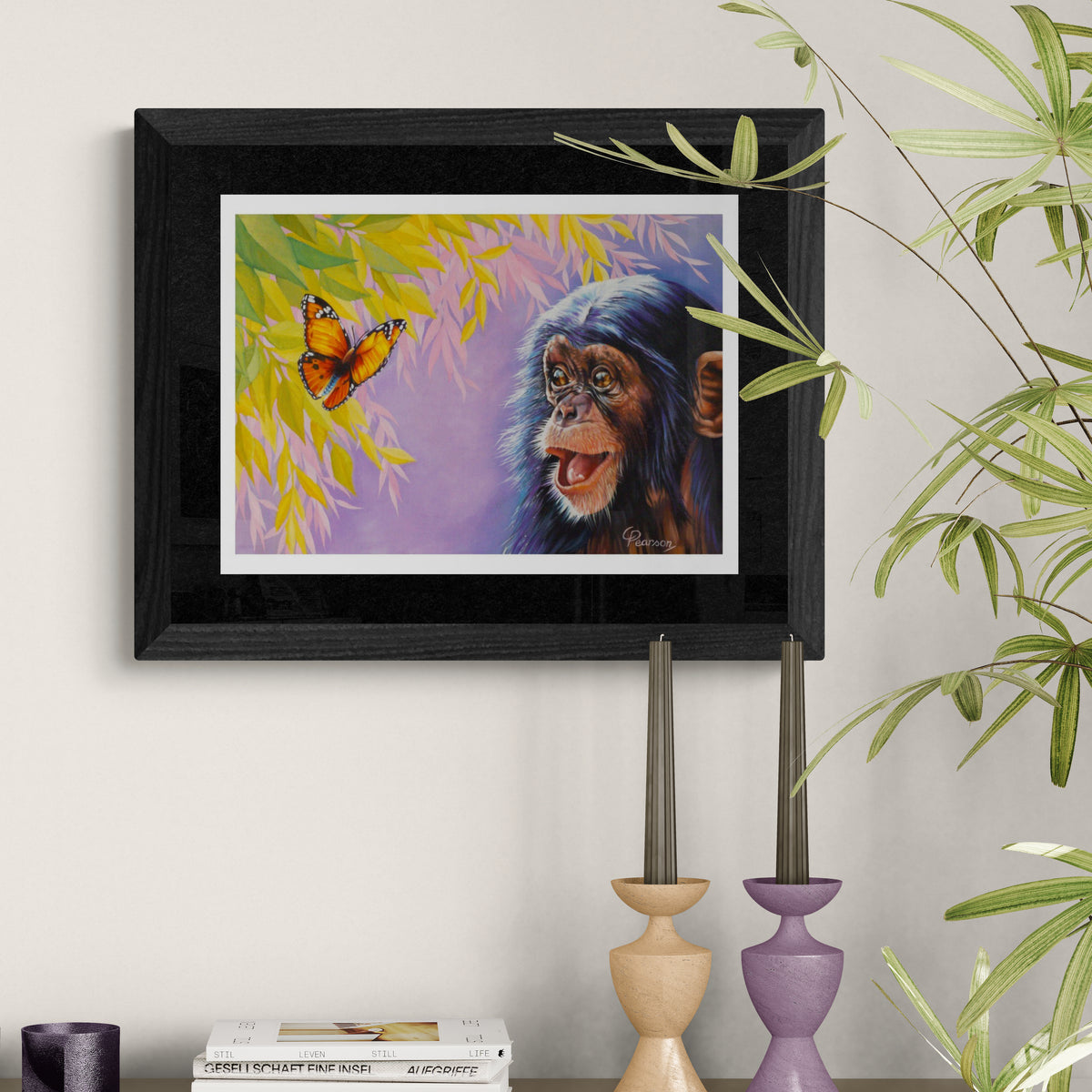 Framed painting of a monkey and butterfly on a wall with decorative candles and books below.