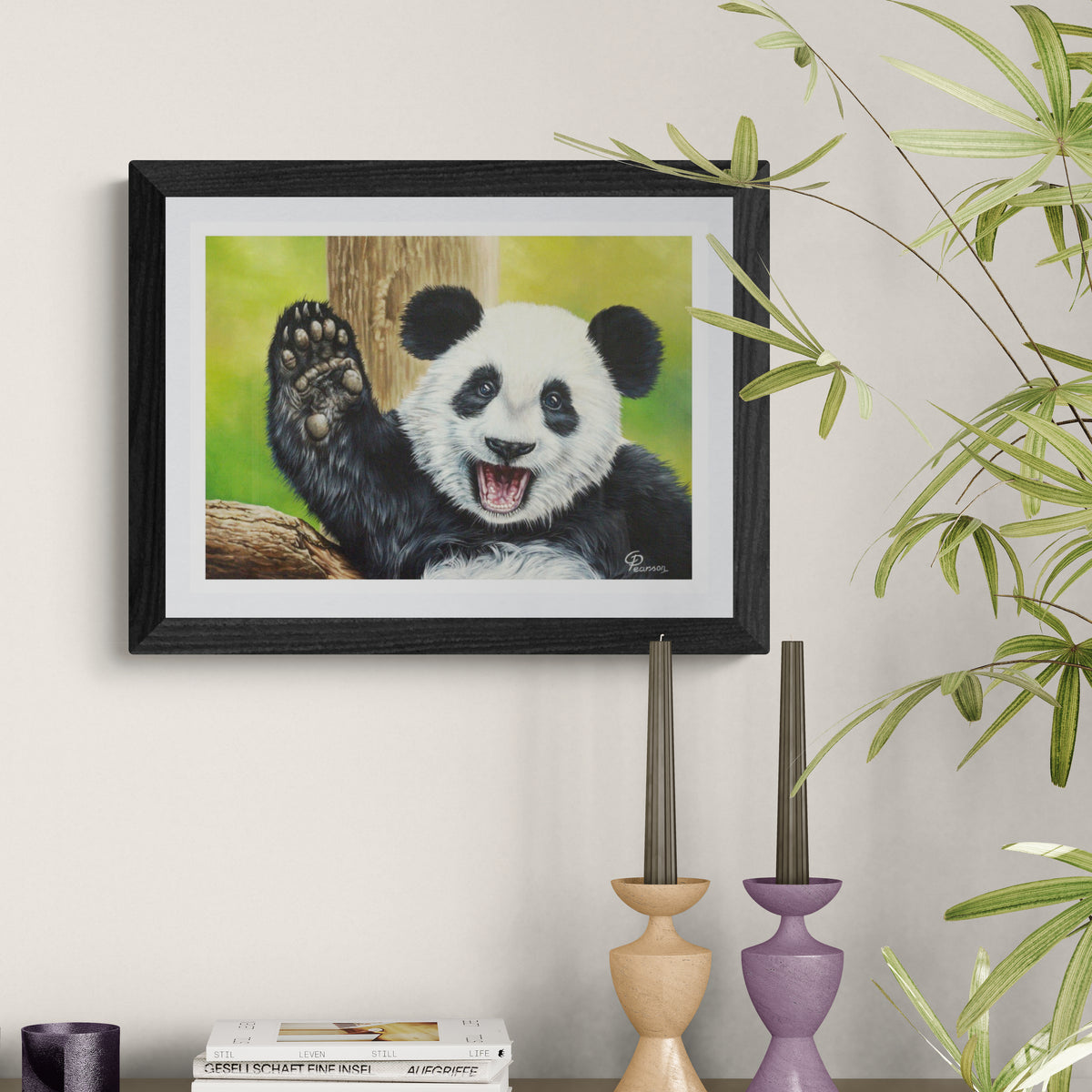 Framed painting of a panda bear on a wall with decorative candles and books below.