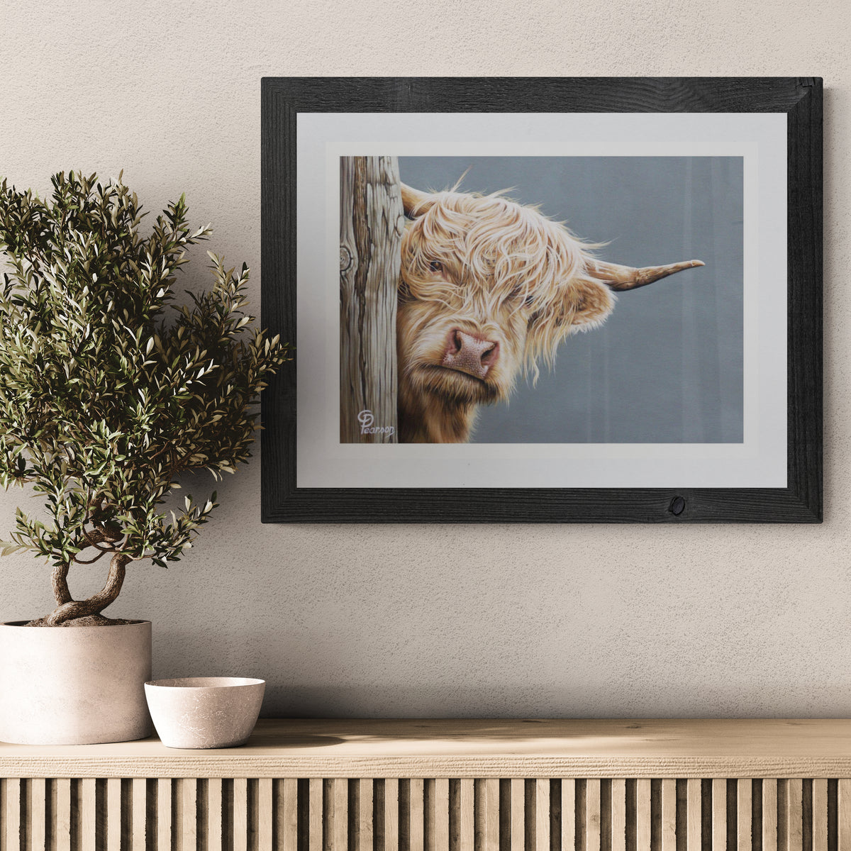 Framed picture of a Highland cow on a wall above a wooden console table with decorative items.