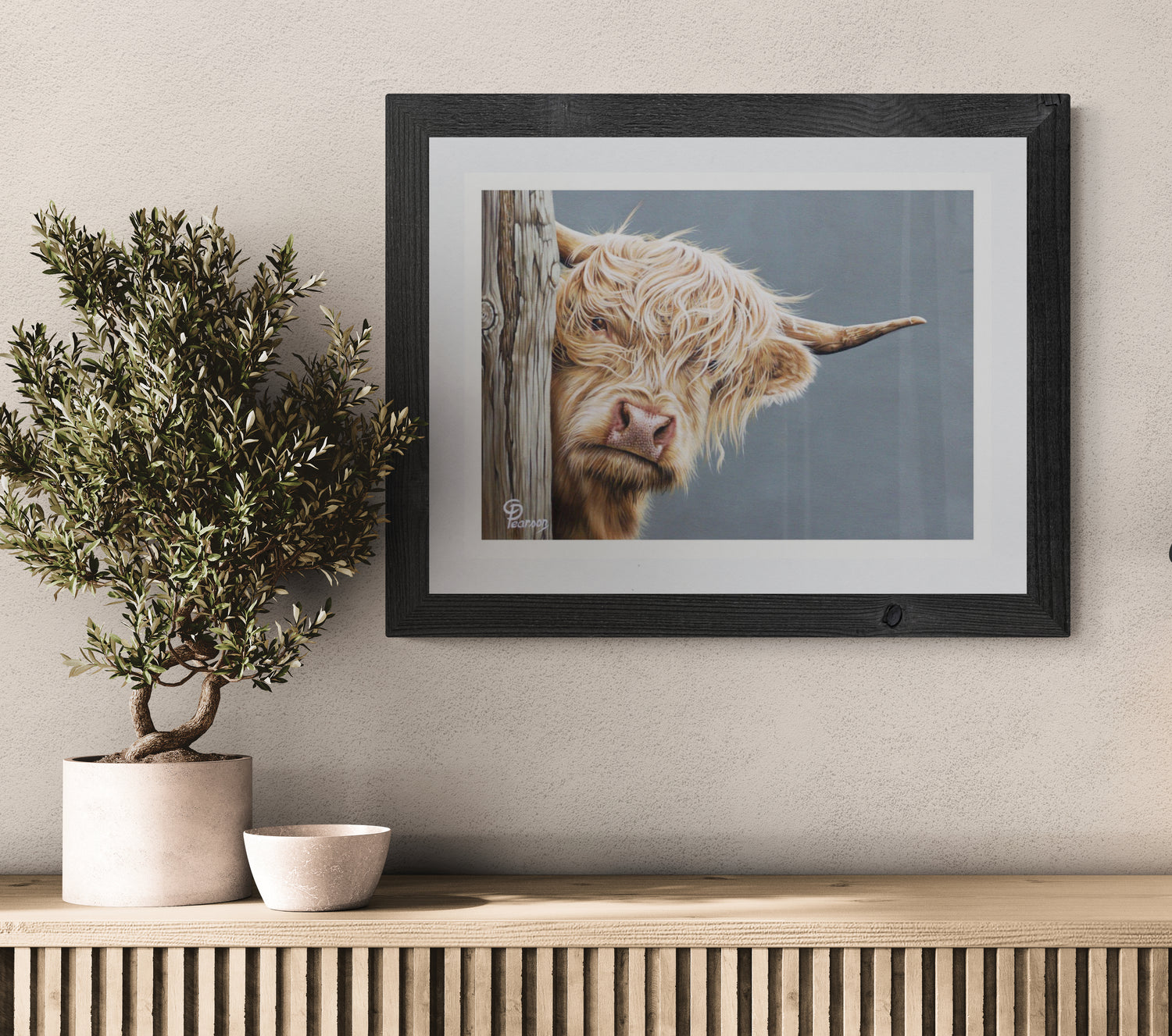 Framed picture of a Highland cow on a wall above a wooden console table with decorative items.