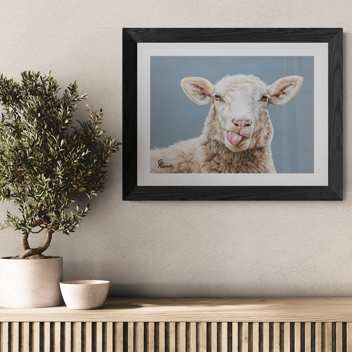Framed picture of a sheep on a wall above a wooden console table with a plant and bowl.